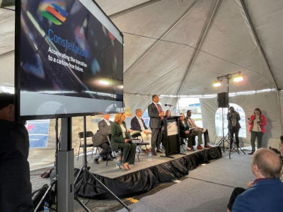 TV monitor on side of presenters on stage inside a tent